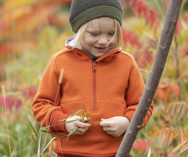 Blond child with the disana orange troyer holds grasses in his hands